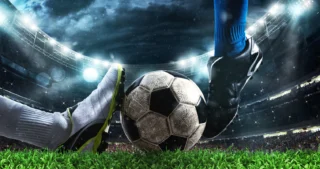 Ballon de football au sol entre deux joueurs sur un terrain éclairé par les projecteurs